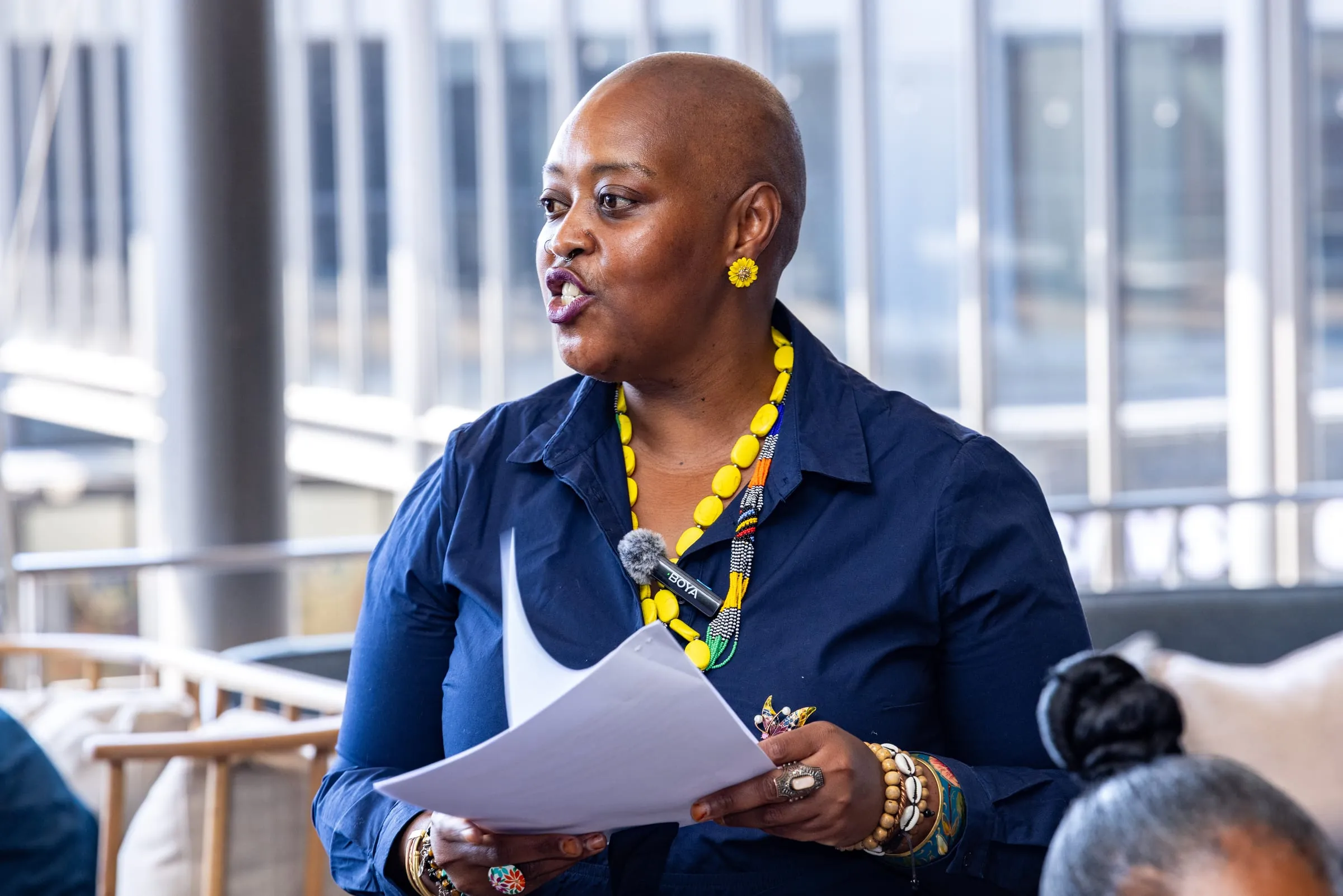 A speaker addresses the table, notes in hand